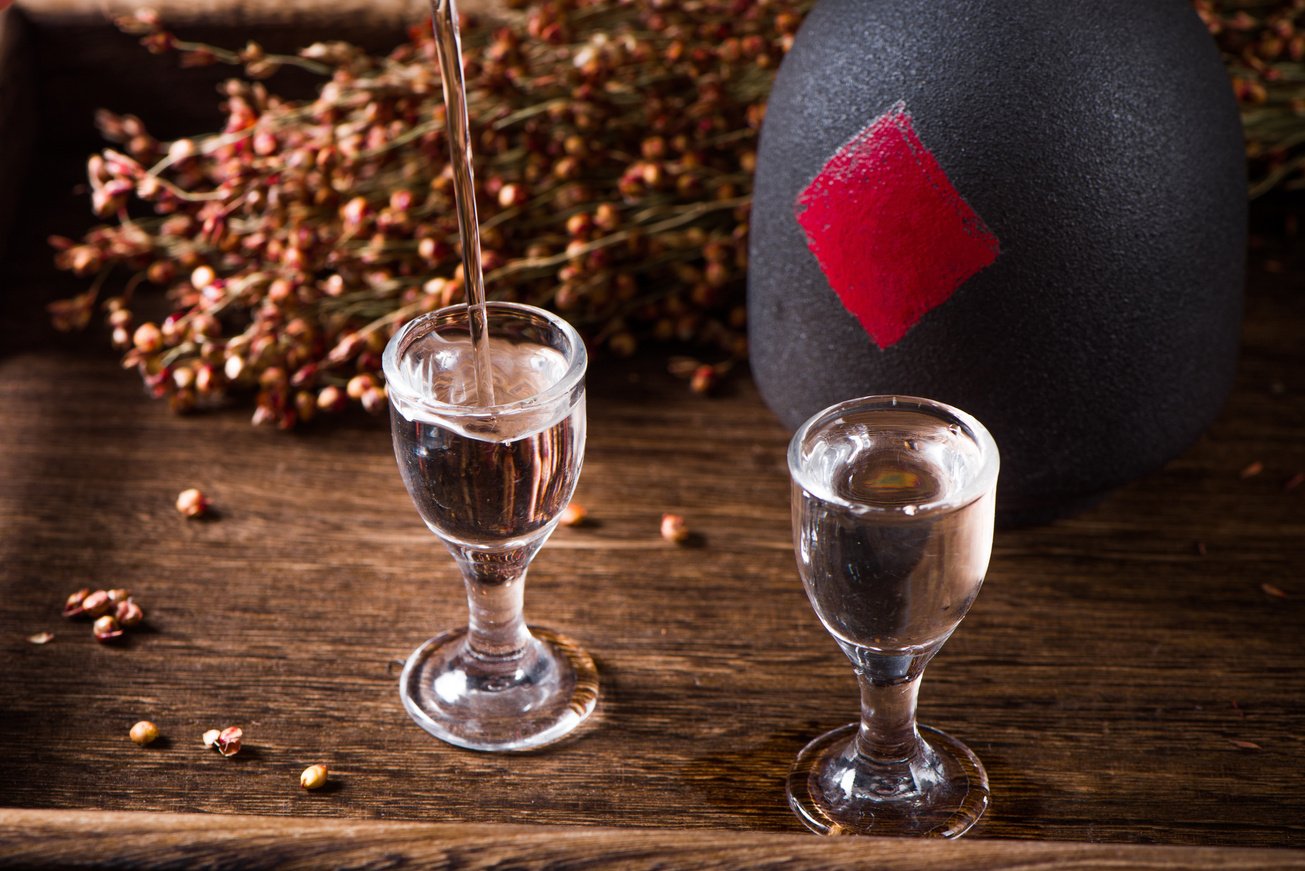 chinese liquor is pouring into a glass from a bottle on wood background