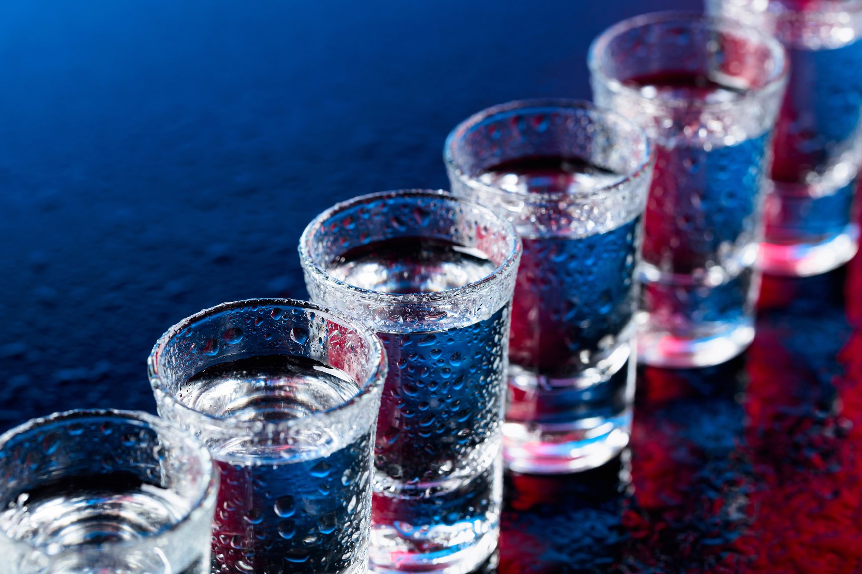 Glasses of vodka on a damp glass table.